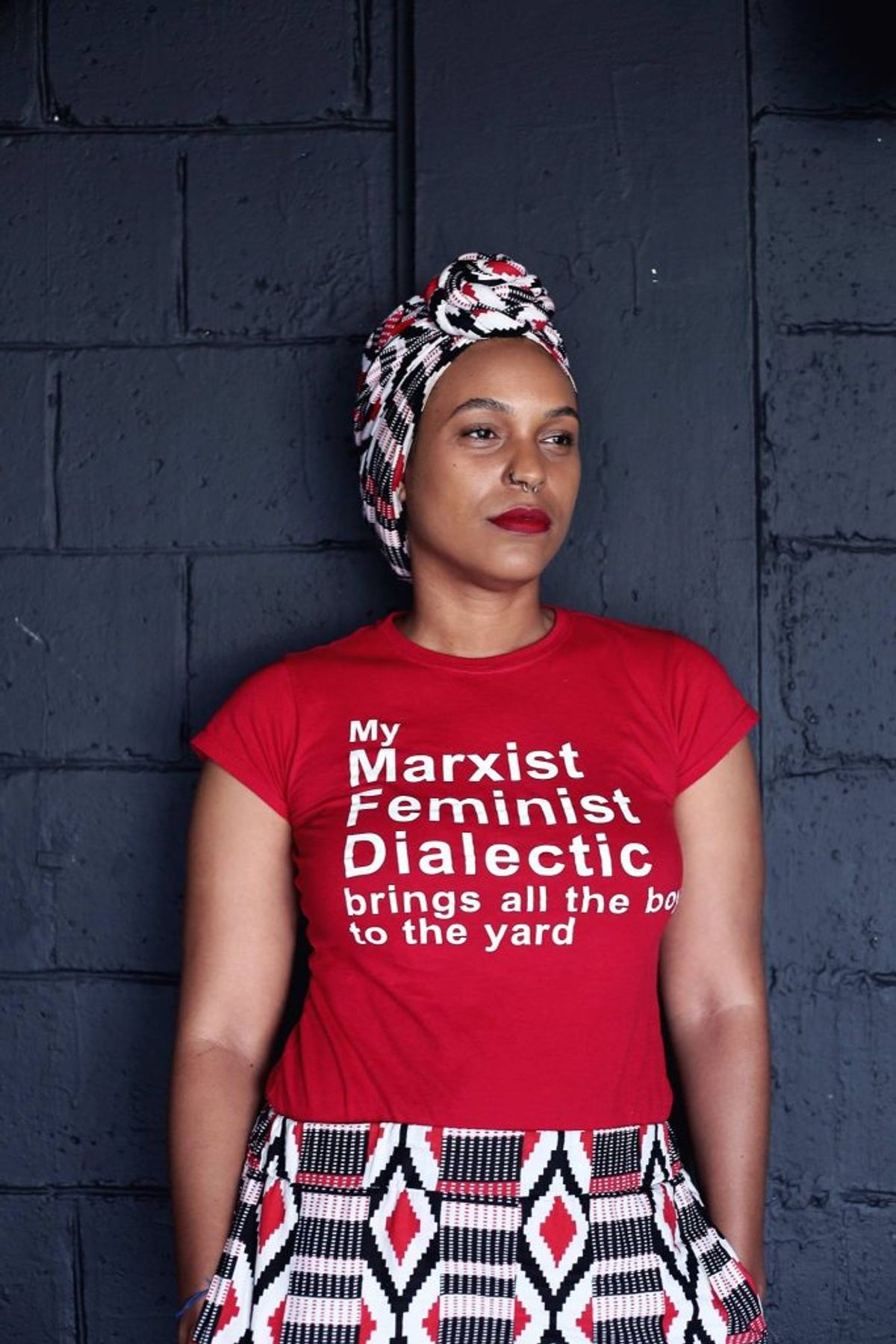 Image of person wearing a red shirt with white text that reads my marxist feminist dialectic brings all the boys to the yard